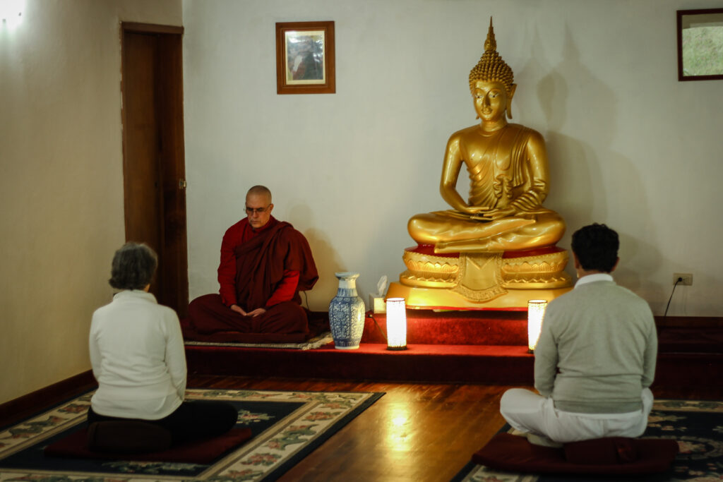 El Venerable Bhikkhu Nandisena y dos personas meditando en el salón, ante la imagen del Buddha.