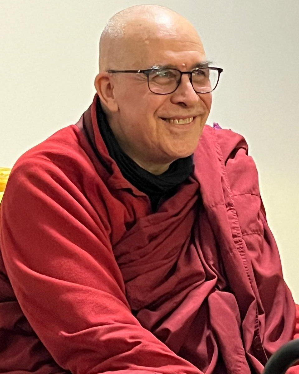 Bhikkhu Nandisena, sonriente, con el hábito granate, sentado durante una clase